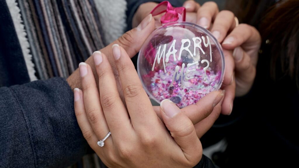 Man proposing to a woman with a diamond engagement ring hidden in a Christmas bubble